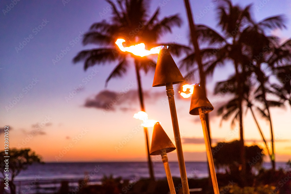 Obraz premium Zachód słońca na Hawajach z pochodniami ognia. Hawajska ikona, światła płonące o zmierzchu w nadmorskim kurorcie lub restauracje do oświetlenia zewnętrznego i dekoracji, przytulna atmosfera.