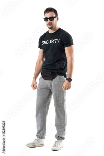 Young police officer in plain sporty clothes with sunglasses looking at camera. Full body length portrait isolated on white studio background. 