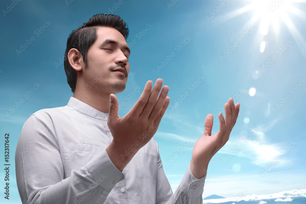 Naklejka premium Handsome asian muslim man raising hand and praying