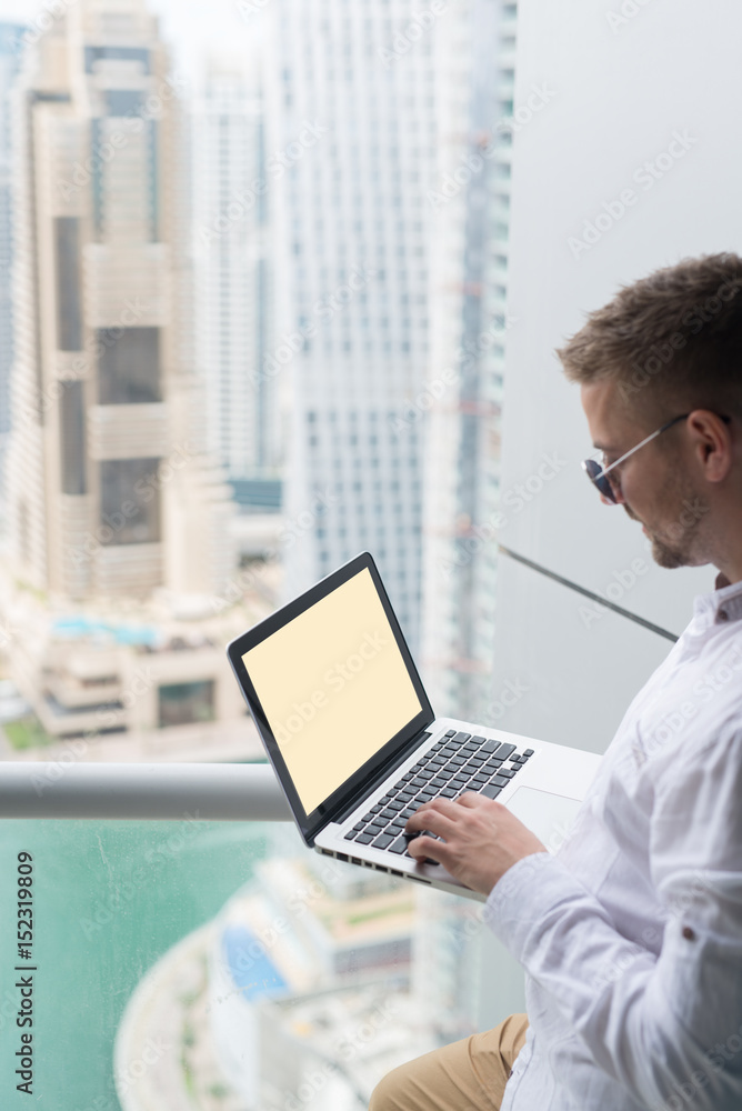 Young businessman working on his laptop, in an office with a beautiful city scape view. Young businessman working on his laptop, in an office with a beautiful city scape view.