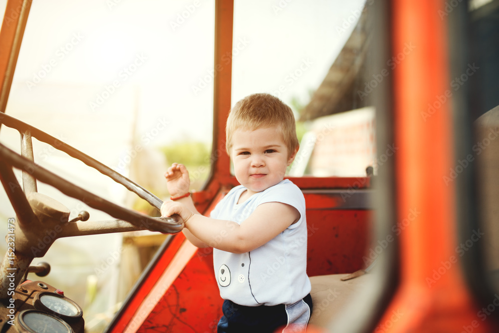 Baby boy holding a steering wheel of tractor. Childhood moments on the countryside. Baby boy holding a steering wheel of tractor. Childhood moments on the countryside.