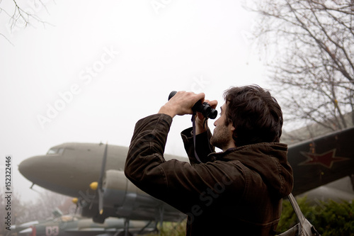 Man looking through the binoculars against aircraft background