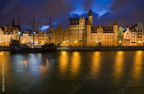 Caravel moored by Long Embankment on Motlawa River in the Old Town of Gdansk, Poland at night. Illuminated Mariacka Gate on the right