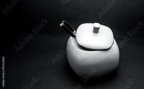 An old sugar bowl with spoon on black background (B/W photo)
