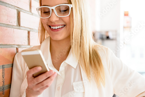 Charming blonde female standing in office with smartphone