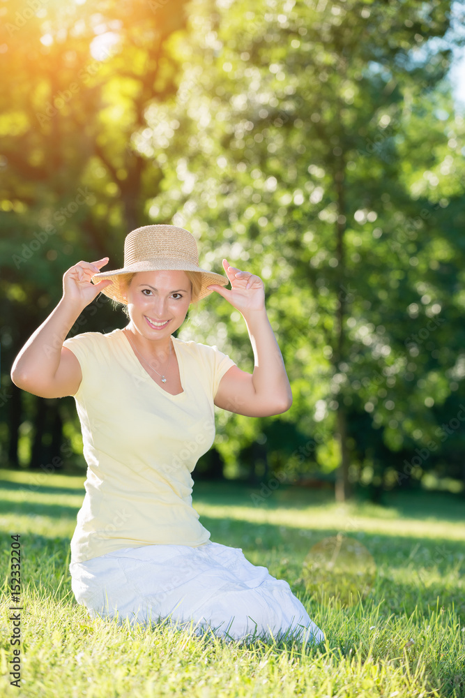 Fototapeta premium Happy, blonde woman with a hat posing in the sunset park.Lens flare
