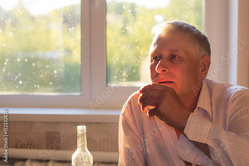 Fotografie The gray-haired man drinks vodka from a glass at home
