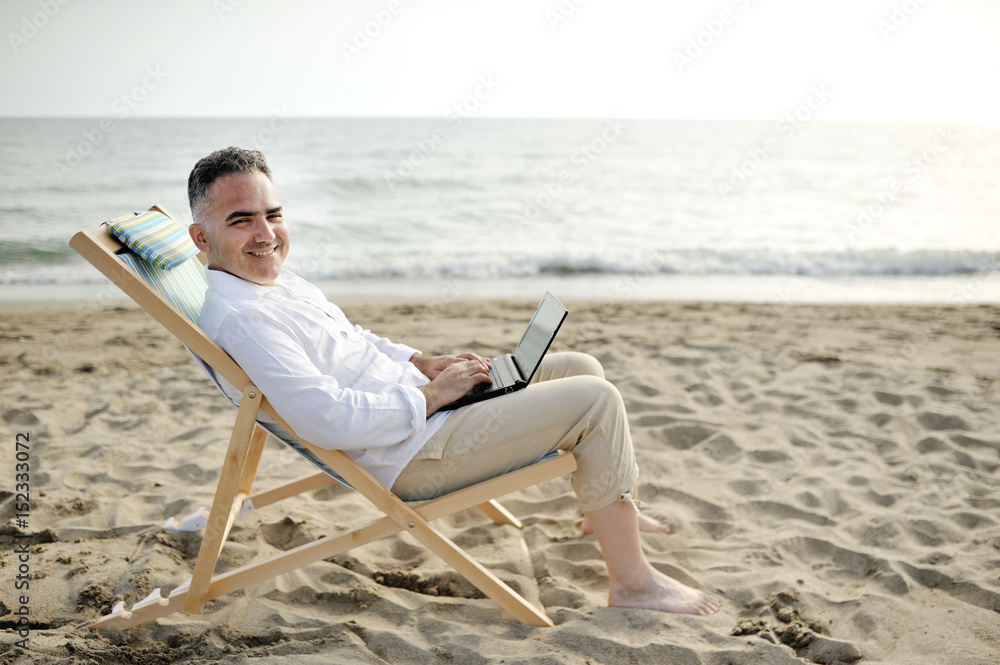 Man with laptop working on the beach sitting on a deckchair