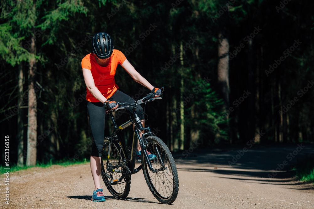 Obraz premium Young pretty woman in helmet and orange shirt sitting on bicycle on the forest road. Healthy lifestyle concept. Sports Girl with bike.