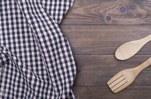 Background of plaid kitchen tablecloth and cutlery on wooden background. Copy space. Horizontal shoot.
