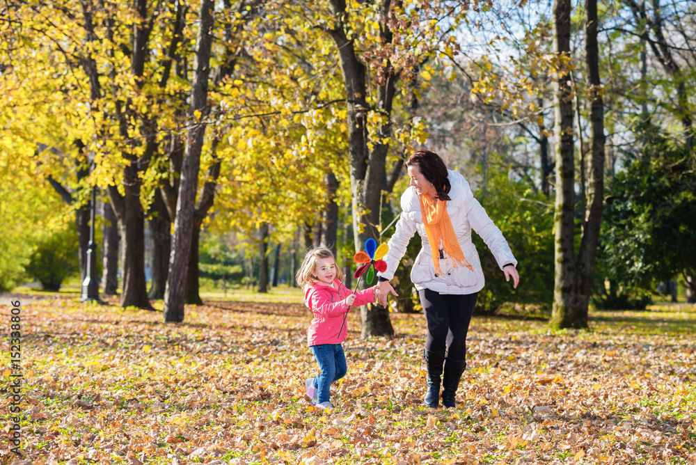 Mother and daughter have a fun with pinwheel in the autumn park.Focus on the child face Mother and daughter have a fun with pinwheel in the autumn park.Focus on the child face