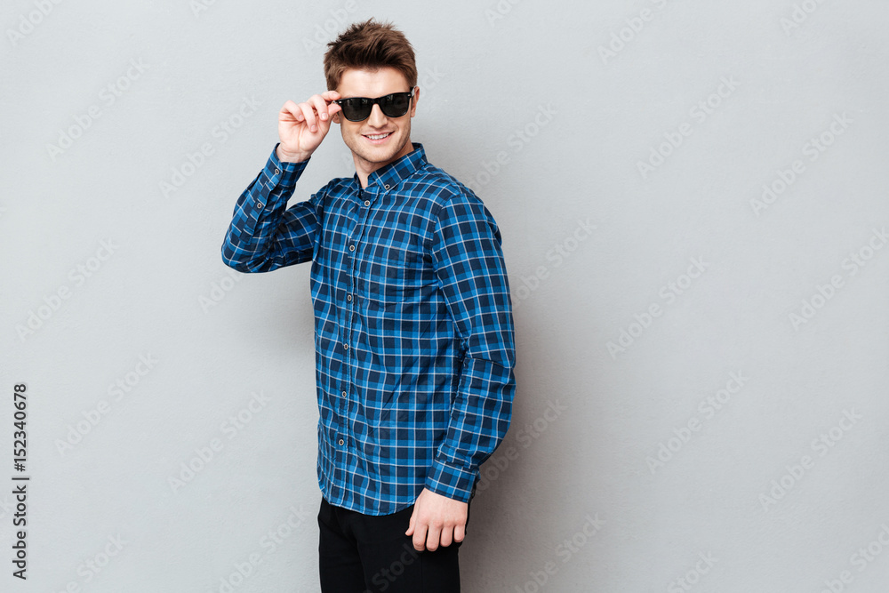 Cheerful man wearing sunglasses standing over grey wall Cheerful man wearing sunglasses standing over grey wall