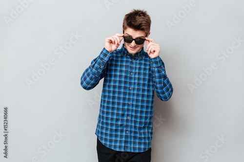Happy man wearing sunglasses standing over grey wall