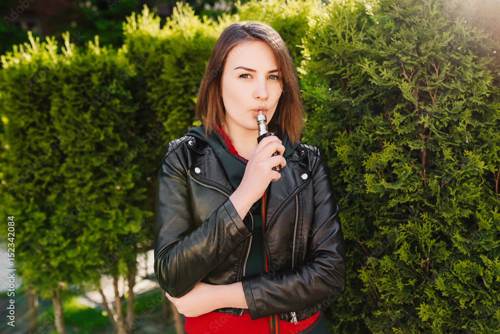 Vaping. Young beautiful girl smoking ( vaping ) e-cigarette with smoke outdoors. Vapor concept. Vaping. Young beautiful girl smoking ( vaping ) e-cigarette with smoke outdoors. Vapor concept.