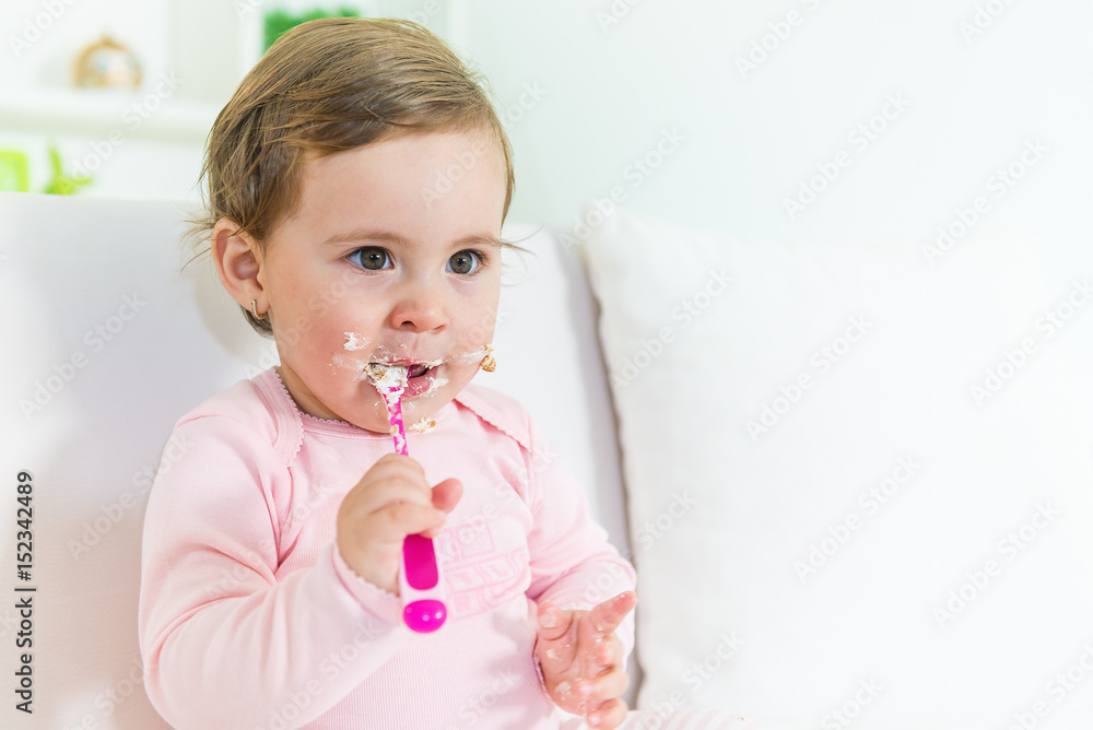 Sweet little baby girl eating her first cake on the sofa.Copy space, shallow doff Sweet little baby girl eating her first cake on the sofa.Copy space, shallow doff