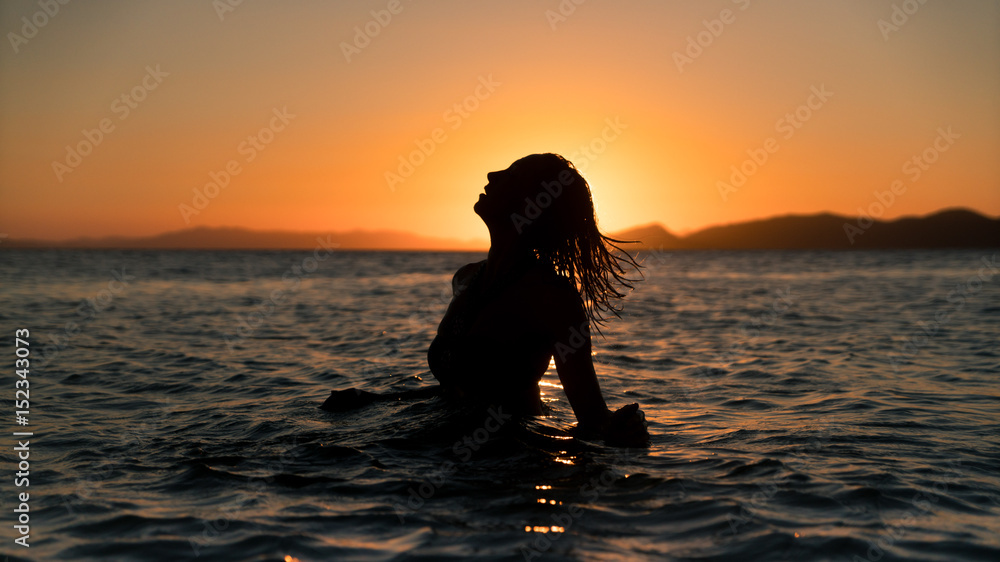 Silhouette girl in ocean during sunset