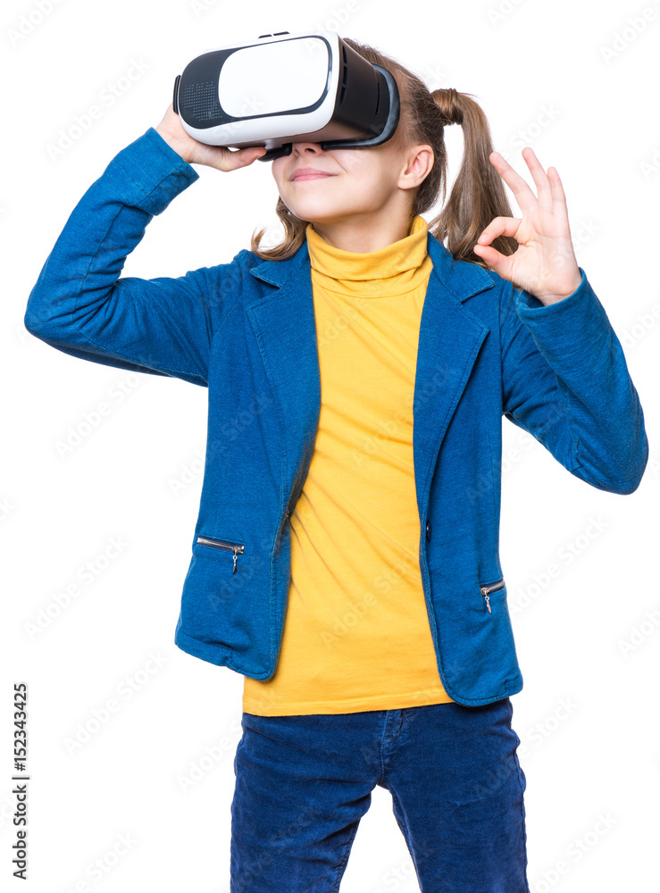 Happy little girl wearing virtual reality goggles watching movies or playing video games, isolated on white background. Cheerful smiling kid looking in VR glasses and making ok gesture.