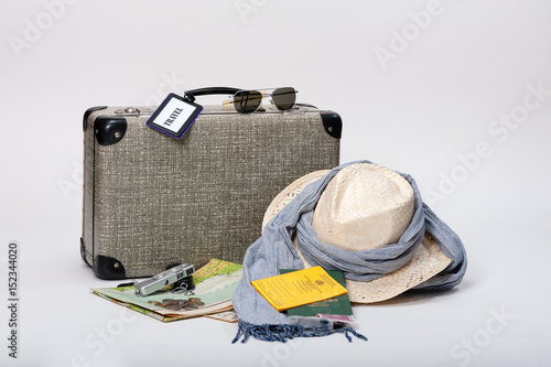 Preparing for a journey. Vintage suitcase with a map, travel documents, a hat, money and sunglasses, displayed on a white background.
