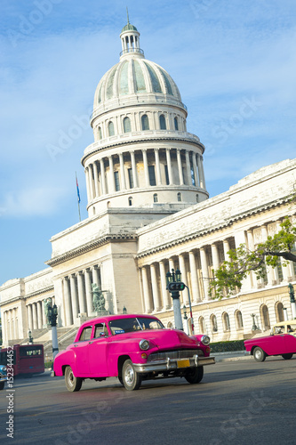 Brightly colored classic American cars serving as taxis pass on the main street in front of the Capitolio building in Central Havana, Cuba