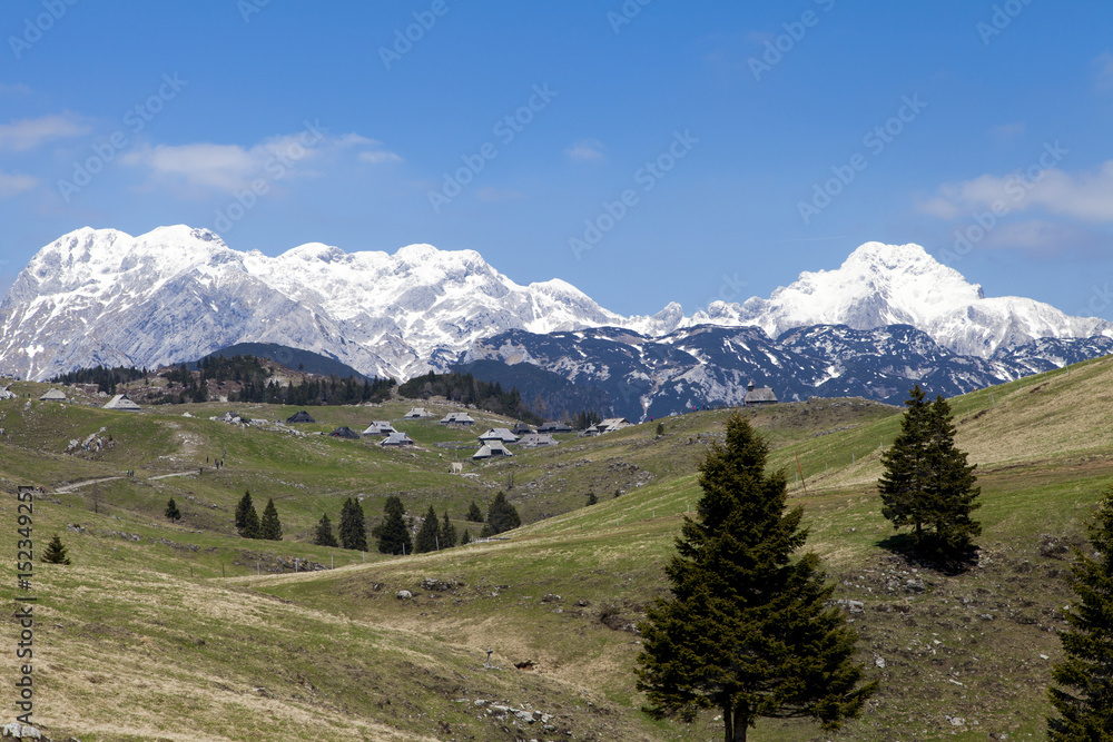 Beautiful view on herdsman village, tableland Velika planina in Slovenia, against blue sky and high mountains covered with snow. Space for text