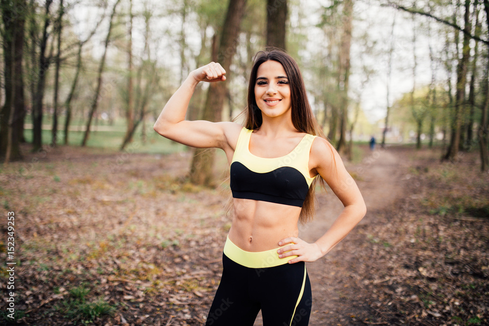Fototapeta premium Fitness girl in park showing biceps against park background