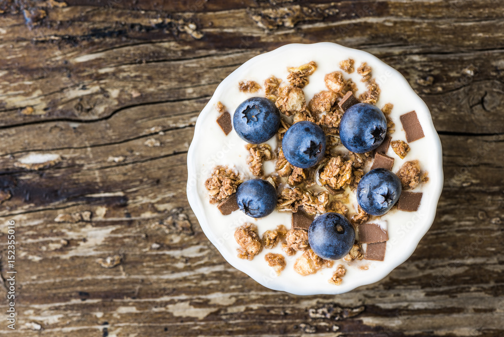 Serving of Yogurt with Whole Fresh Blueberries and Muesli on Old Rustic Wooden Table. Closeup Detail. Serving of Yogurt with Whole Fresh Blueberries and Muesli on Old Rustic Wooden Table. Closeup Detail.
