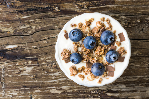 Serving of Yogurt with Whole Fresh Blueberries and Muesli on Old Rustic Wooden Table. Closeup Detail.