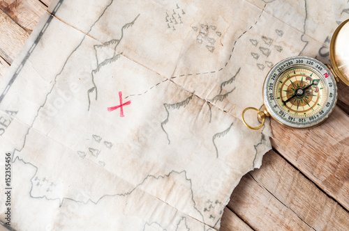 Top view to vintage fake treasure map with red cross and compass on wooden desk