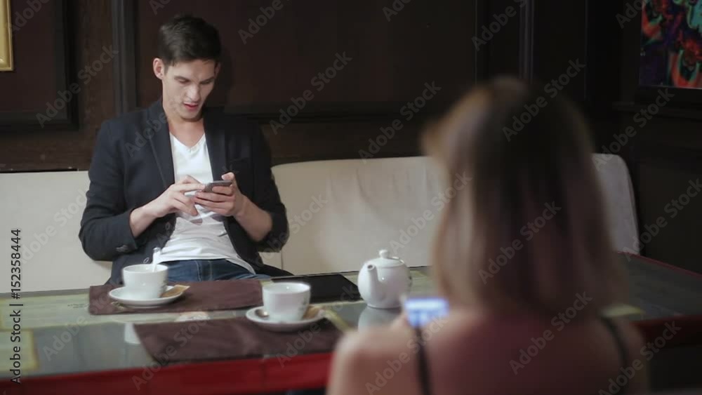 Young beautiful couple sitting in a cafe browsing Internet on their smartphones using Wi-Fi Young beautiful couple sitting in a cafe browsing Internet on their smartphones using Wi-Fi