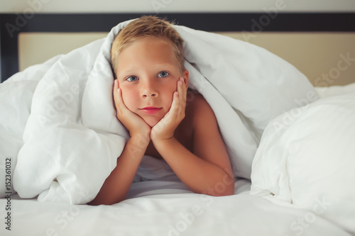 Wallpaper Mural A beautiful white boy lies under a blanket propped his head in his hands and smiles Torontodigital.ca