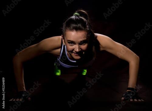 Fitness sexy girl on a dark background. Athlete doing exercises in the gym