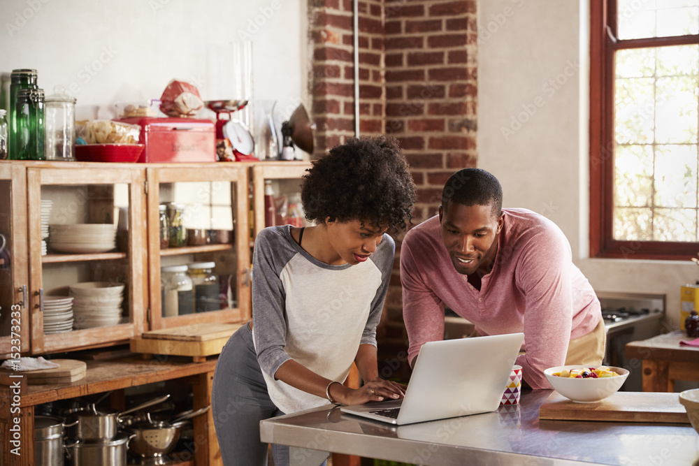 Mixed race couple using laptop computer in their kitchen Mixed race couple using laptop computer in their kitchen