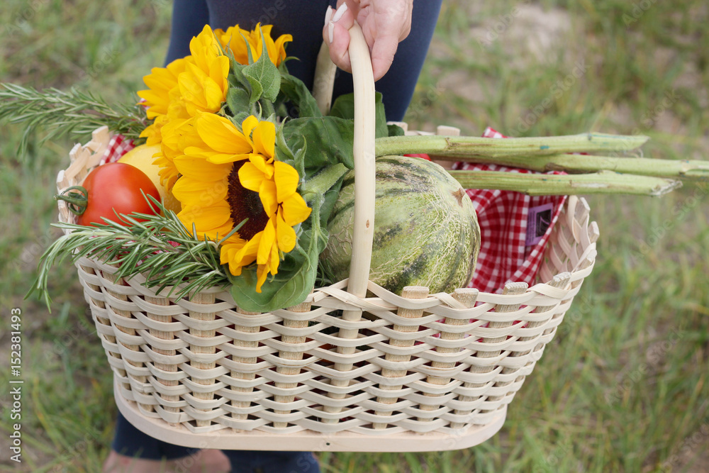 A wooden basket with sunflowers and fresh vegetables in standing on the ground. A wooden basket with sunflowers and fresh vegetables in standing on the ground.