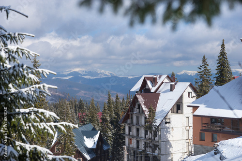 Obraz na płótnie Winter mountains near cottages between snow-covered fir-trees, focus on branch of a tree w salonie