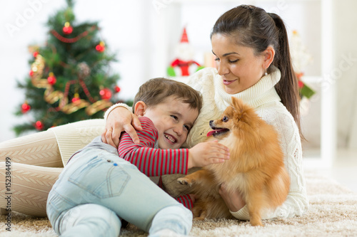 smiling family and dog sitting by Christmas tree