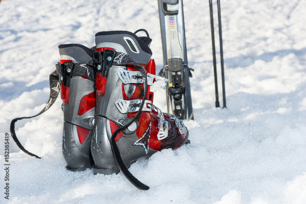 Close up of red and gray boots next to ski laying in fluffy snow in a ski-resort