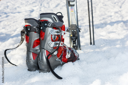Obraz na płótnie Close up of red and gray boots next to ski laying in fluffy snow in a ski-resort w salonie