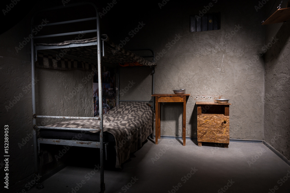 Jail cell with iron bunk bed and wooden bedside table