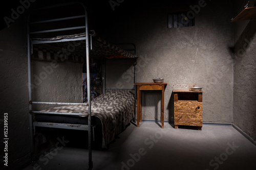 Obraz na płótnie Jail cell with iron bunk bed and wooden bedside table w salonie