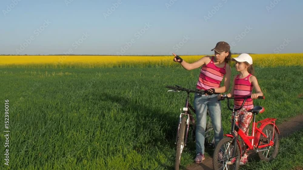 A woman with a child on bicycles in the countryside. A sports family in nature. Mom and daughter on bicycles in the field. Active family vacation. Mom shows the way to the child. Slow-motion shooting. A woman with a child on bicycles in the countryside. A sports family in nature. Mom and daughter on bicycles in the field. Active family vacation. Mom shows the way to the child. Slow-motion shooting.