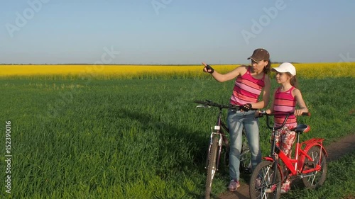A woman with a child on bicycles in the countryside. A sports family in nature. Mom and daughter on bicycles in the field. Active family vacation. Mom shows the way to the child. Slow-motion shooting. photo