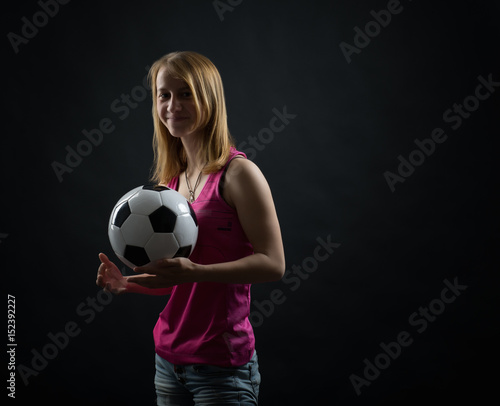 Soccer player teen girl with a soccer ball posing in studio. © kulichok