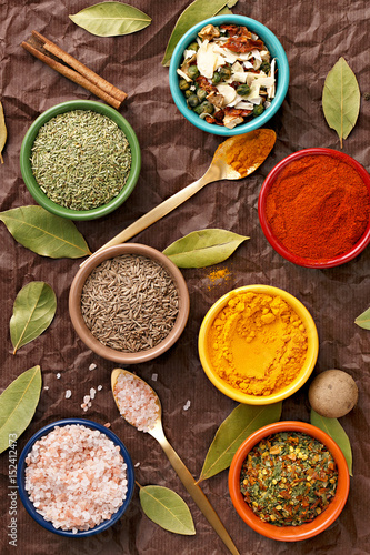 Fototapeta Naklejka Na Ścianę i Meble -  Spices in colorful bowls viewed from above. Various seasonings on a dark background. Italian mix, cumin, chili pepper, curry powder, Himalayan salt, pepper, garlic, cinnamon, dried tomato. Top view