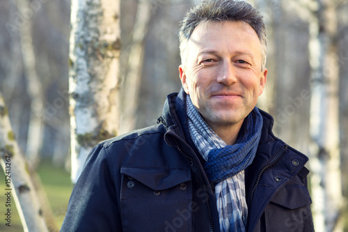 Handsome happy smiling man. Outdoor autumn male portrait. Attractive confident middle-aged man posing in city park, birch grove.