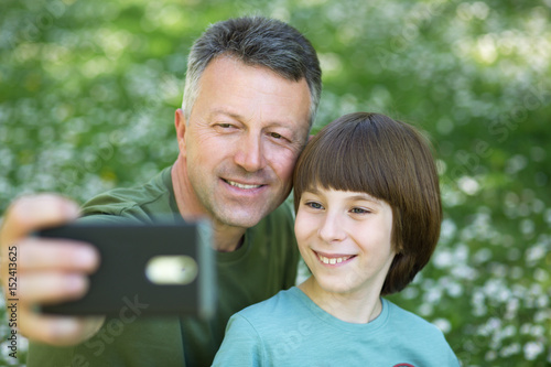 Father and son taking photo with smartphone together outdoor. Family selfie time. photo