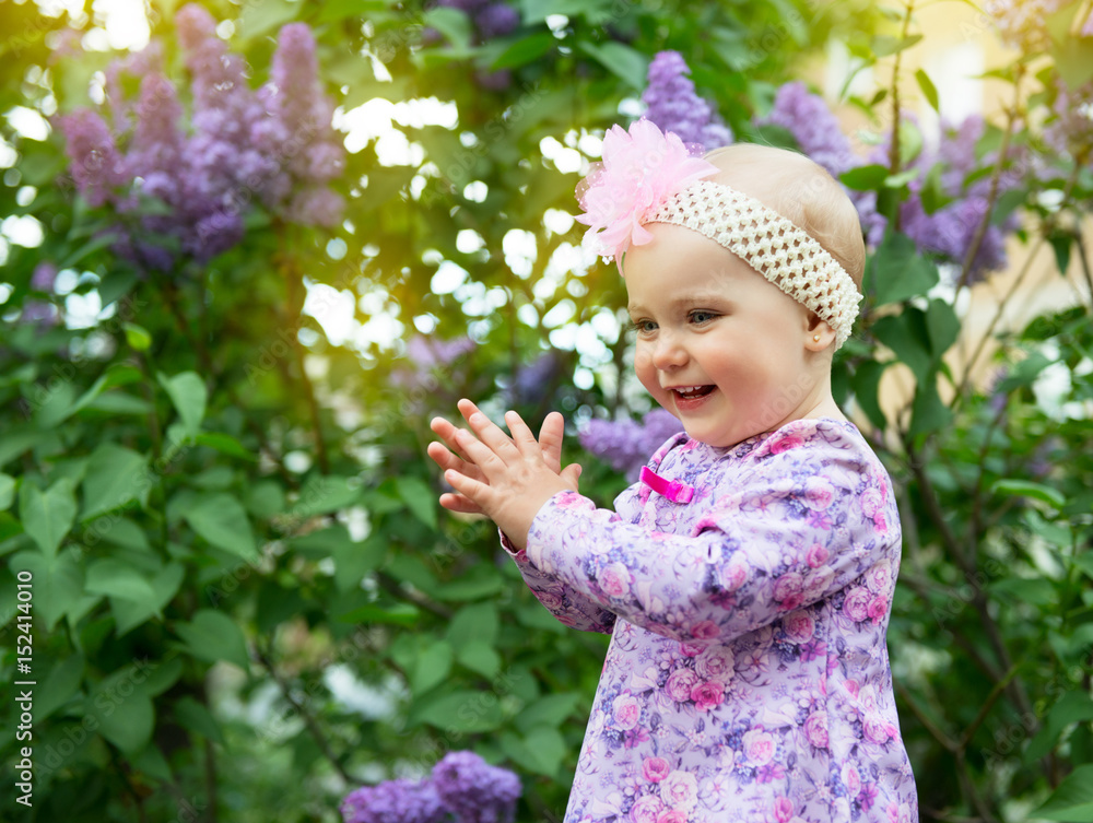 Beautiful little girl happy smiling and claps her hands over lilac flowers in spring park. Childhood. Cute kid's face over nature background. Cheerful child's portrait, soft focus. Beautiful little girl happy smiling and claps her hands over lilac flowers in spring park. Childhood. Cute kid's face over nature background. Cheerful child's portrait, soft focus.