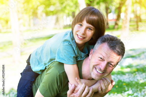 Portrait of father with his son having fun in summer park. Piggyback. Family fun. Happy boy playing with dad summer nature outdoor photo