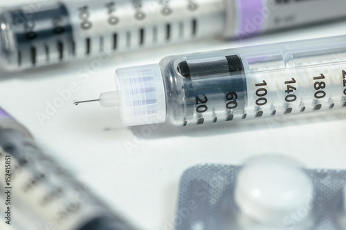 Insulin pen with a drop on needle's tip beside other diabetes medicines, on white