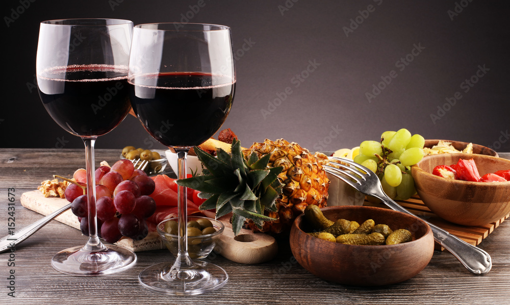 Italian antipasti wine snacks set. Cheese variety, Mediterranean olives, pickles, Prosciutto di Parma with grapes, wine in glasses over black grunge background Italian antipasti wine snacks set. Cheese variety, Mediterranean olives, pickles, Prosciutto di Parma with grapes, wine in glasses over black grunge background