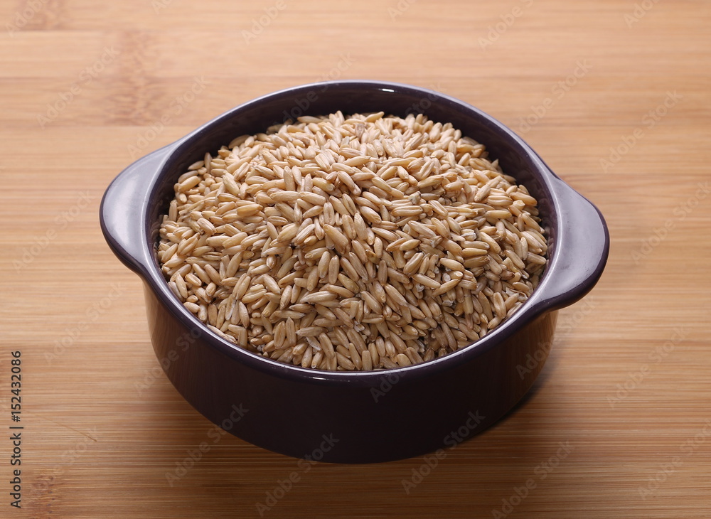 Oat grains in porcelain bowl on wooden rattan bamboo table Oat grains in porcelain bowl on wooden rattan bamboo table